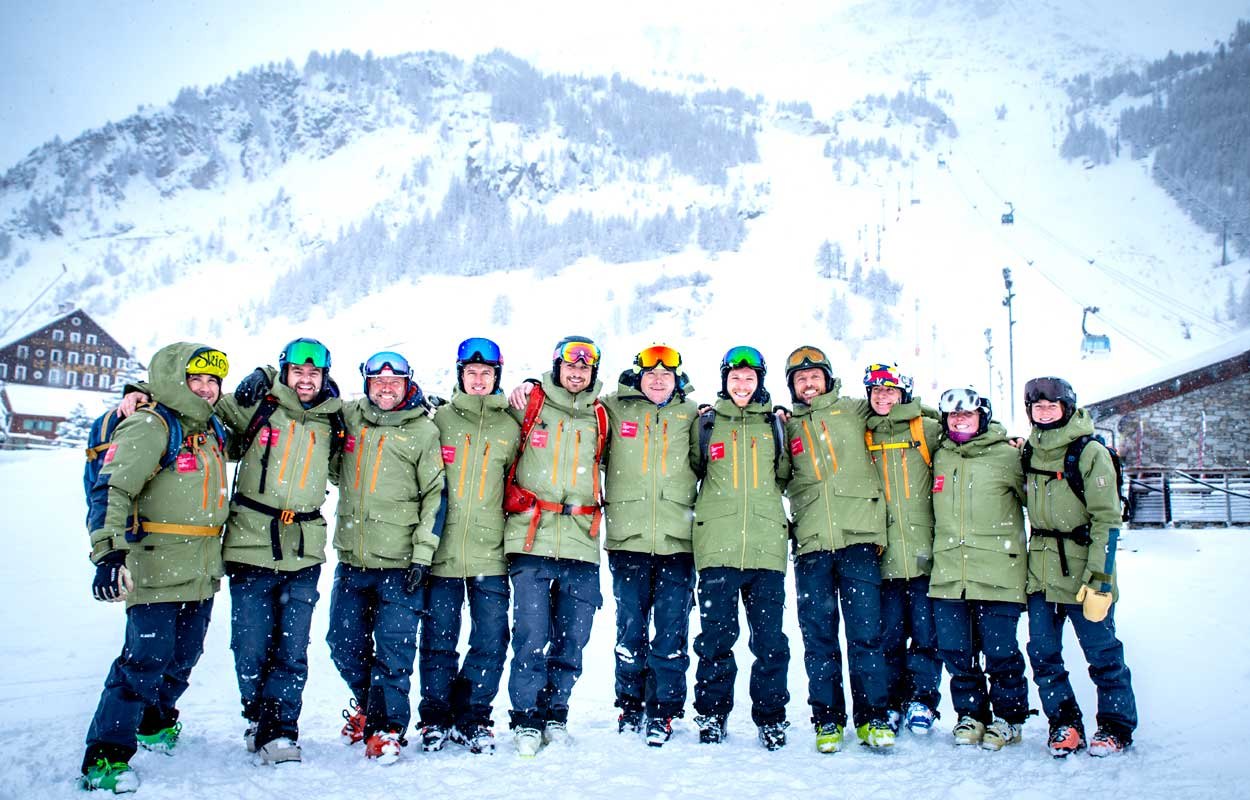 A ski school team lined up arm-in-arm in falling snow at the base of the lifts