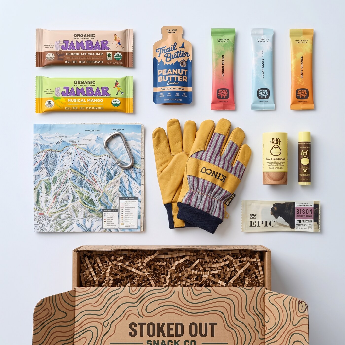 A Stoked Out box laid out with bars, electrolyte sticks, work gloves, sunscreen and a resort map