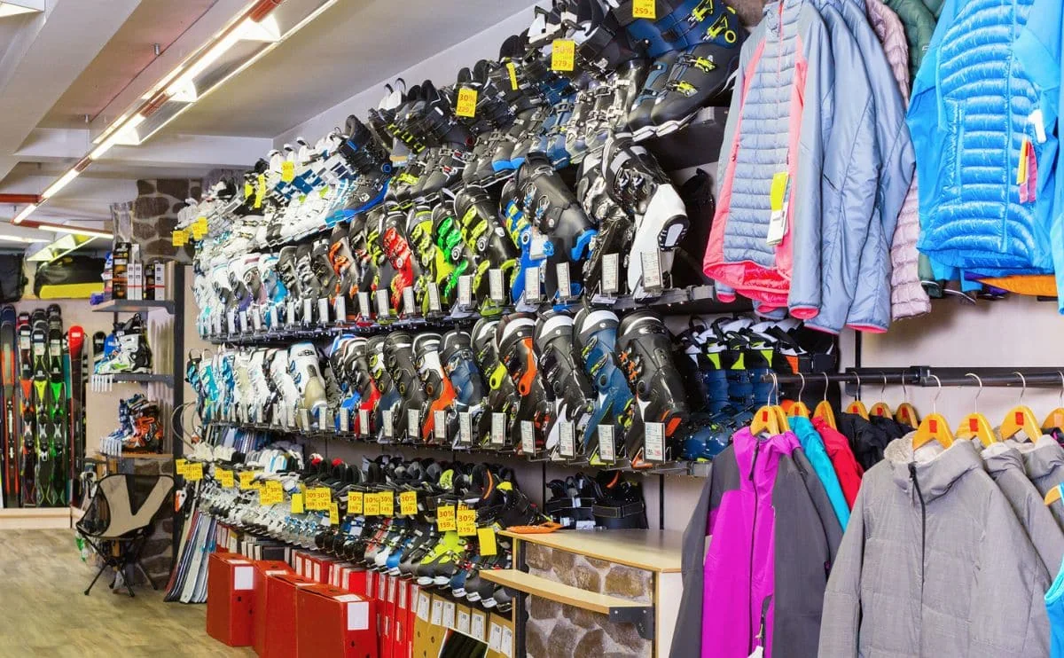 A ski shop wall lined with rows of ski boots beside racks of insulated jackets