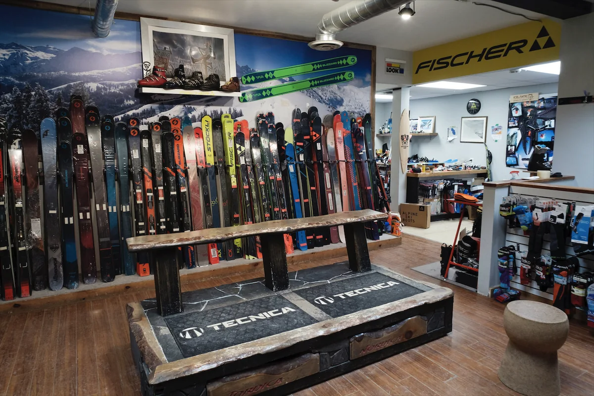 Inside an independent ski shop: skis racked along a mountain mural, a bootfitting bench, and accessories on slatwall