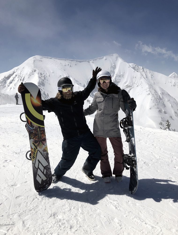 Bass and Madie celebrating on a summit with their snowboards